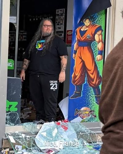 Shop manager standing beside a Goku poster in his looted store in Nice, France